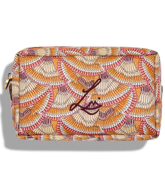 A rectangular beauty bag on a white background. The bag is made using Liberty print fabric which looks like overlapping fans that have brown, beige, orange, white and pink stripes. Lisa Eldridge’s logo is embroidered on the front and the bag has a gold circular zip.