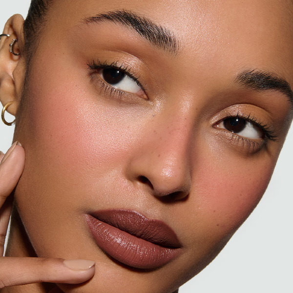 Close-up of a model's face with a neutral background, the model is weating Rae Rouge Experience and a pink blush