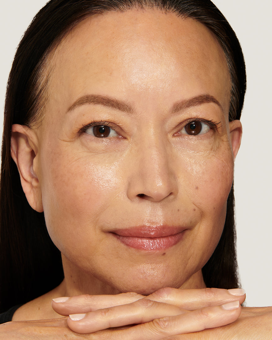 Model with a warm smile, crossing her hands over against a neutral background, wearing Epanoui Baume Embrace