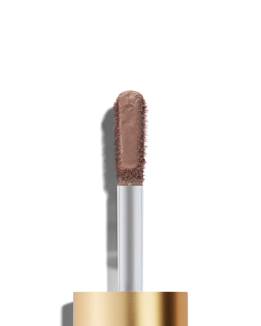 The end of a gold cap containing an applicator wand with a cool mauve Liquid Silk eyeshadow on it, against a white background.