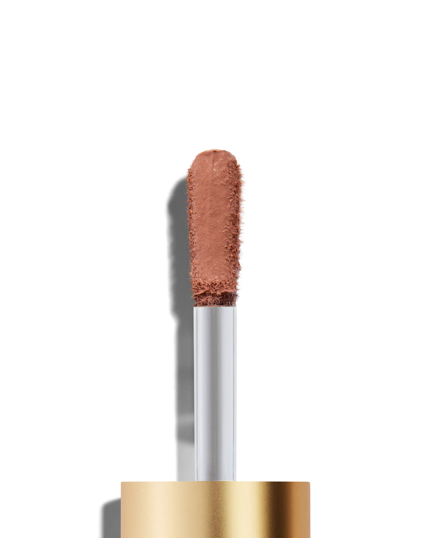 The end of a gold cap containing an applicator wand with a peachy beige Liquid Silk eyeshadow Irene on it, against a white background.