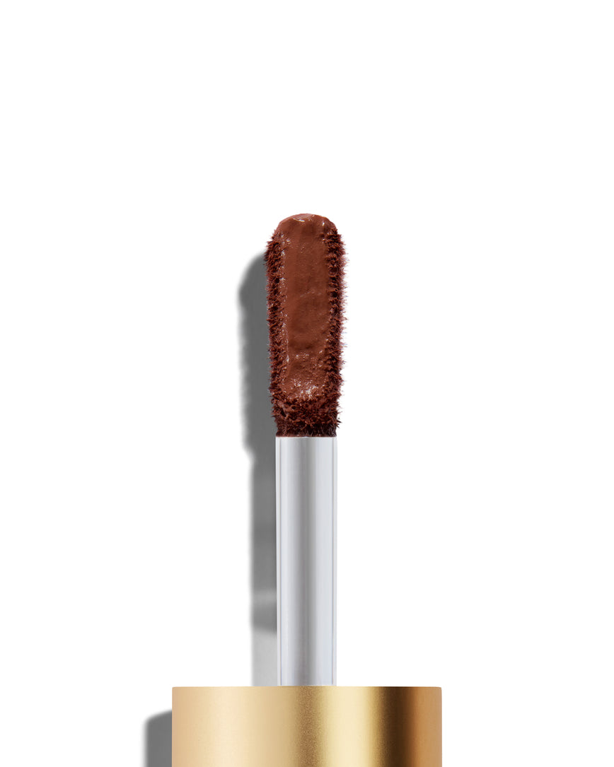 The end of a gold cap containing an applicator wand with a deep rosewood Liquid Silk eyeshadow on it, against a white background.