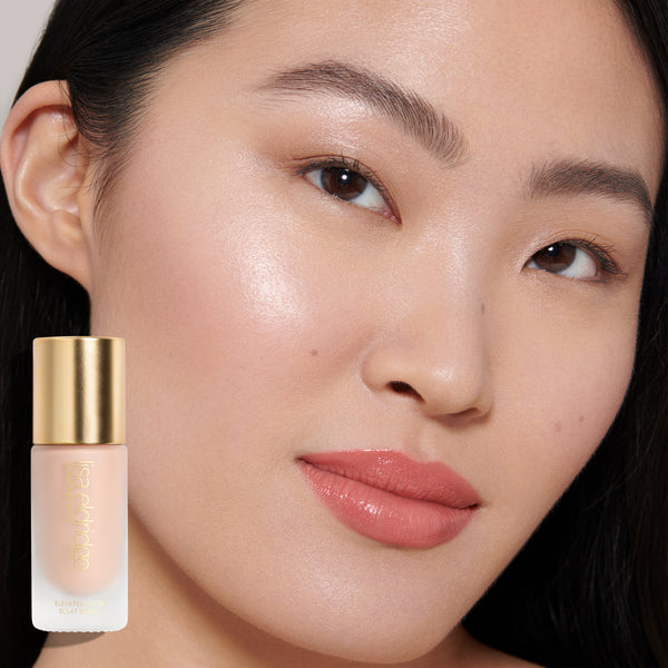 Model wearing Elevated Glow Highlighter with the product in the foreground, on a neutral background