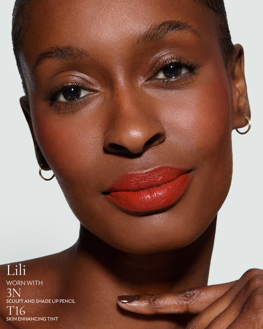 Close-up of a woman with a grey background, focusing on the lip colour - chilli-red Lili, with notes on the 3N Sculpt and Shade Pencil and T16 Skin Enhancing Tint