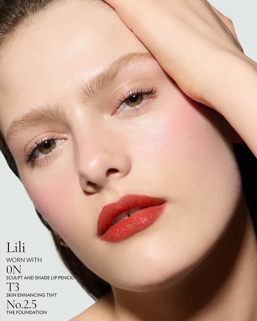 Close-up of a woman with a grey background, focusing on the lip colour - chilli-red Lili, with notes on the 0N Sculpt and Shade Pencil and T3 Skin Enhancing Tint, 2.5 Foundation
