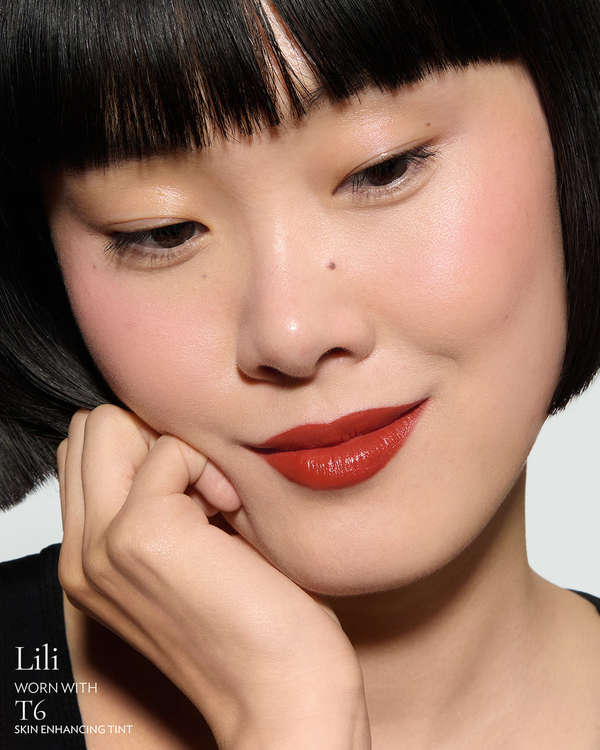 Close-up of a woman with a grey background, focusing on the lip colour - chilli-red Lili, with notes on the T6 Skin Enhancing Tint