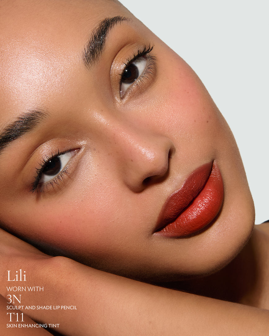 Close-up of a woman with a grey background, focusing on the lip colour - chilli-red Lili, with notes on the 3N Sculpt and Shade Pencil and T11 Skin Enhancing Tint