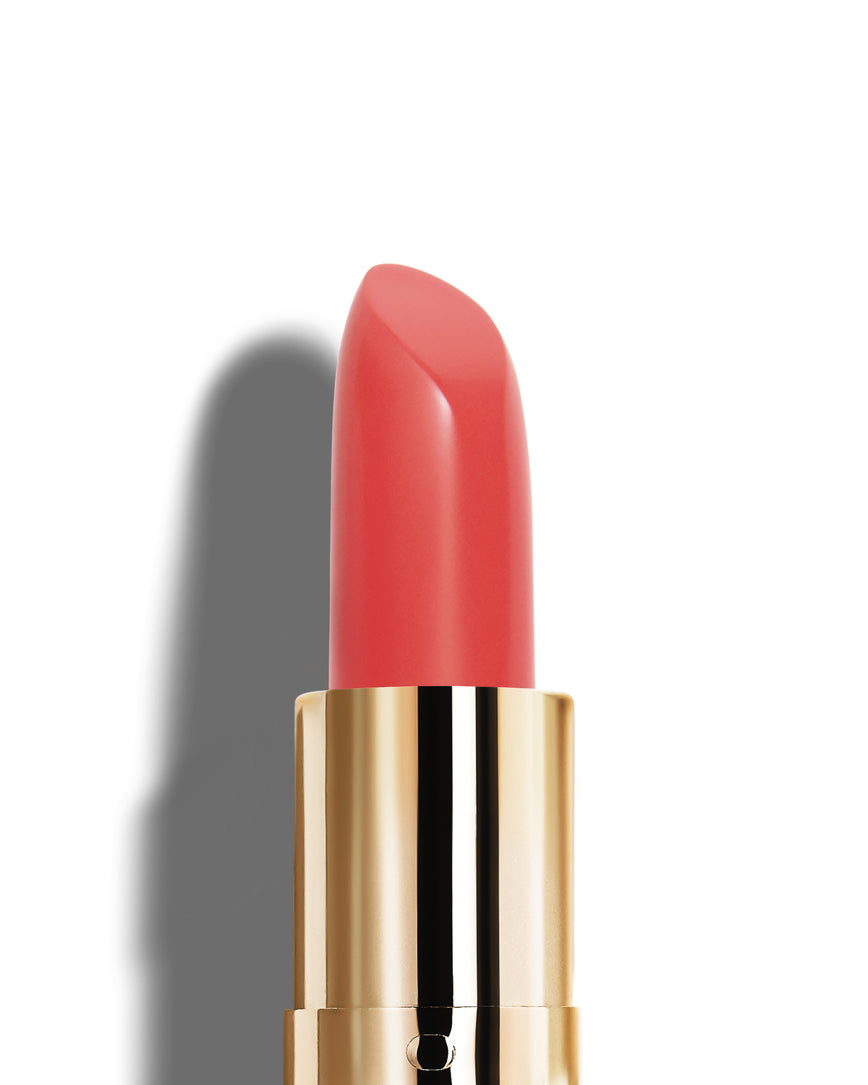Salmon pink lipstick with gold casing on a white background