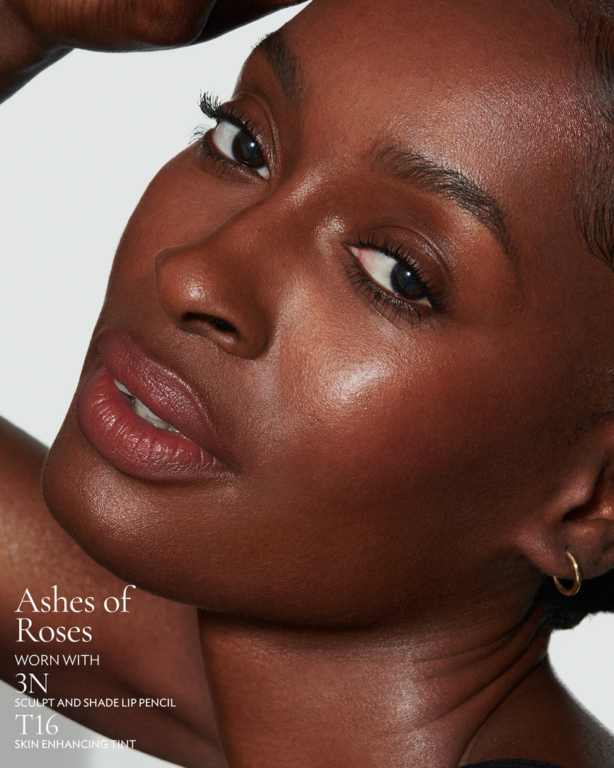 Close-up of a woman with a grey background, focusing on the lip colour - earthy rose Ashes of Roses, with notes on the 3N Sculpt and Shade Pencil and T16 Skin Enhancing Tint