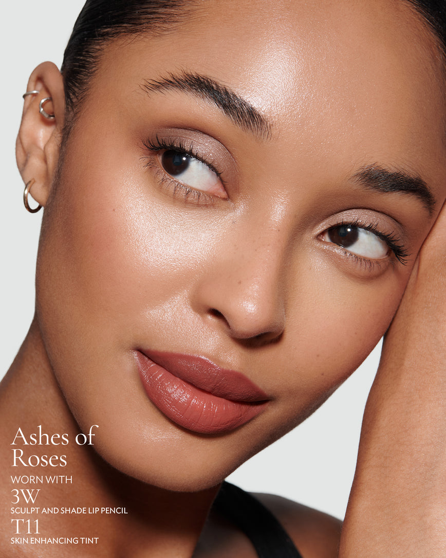 Close-up of a woman with a grey background, focusing on the lip colour - earthy rose Ashes of Roses, with notes on the 3W Sculpt and Shade Pencil and T11 Skin Enhancing Tint