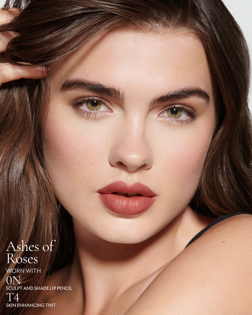 Close-up of a woman with a grey background, focusing on the lip colour - earthy rose Ashes of Roses, with notes on the 0N Sculpt and Shade Pencil and T4 Skin Enhancing Tint