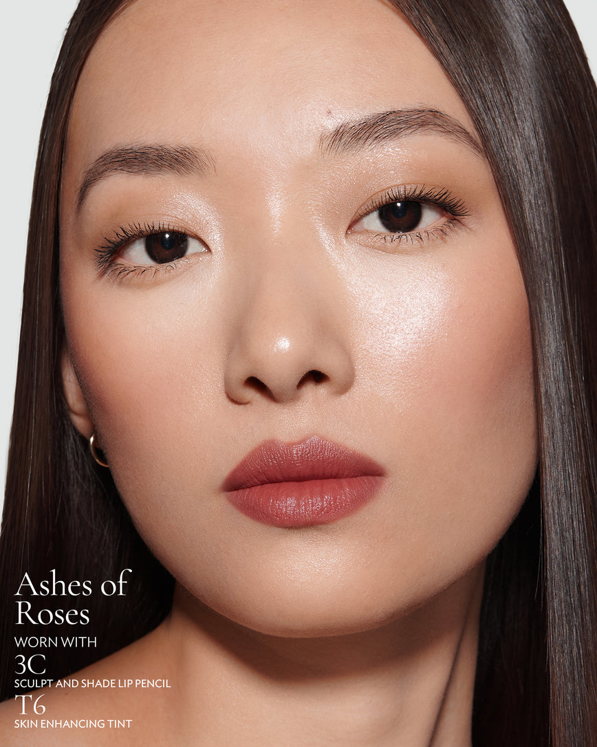 Close-up of a woman with a grey background, focusing on the lip colour - earthy rose Ashes of Roses, with notes on the 3C Sculpt and Shade Pencil and T6 Skin Enhancing Tint