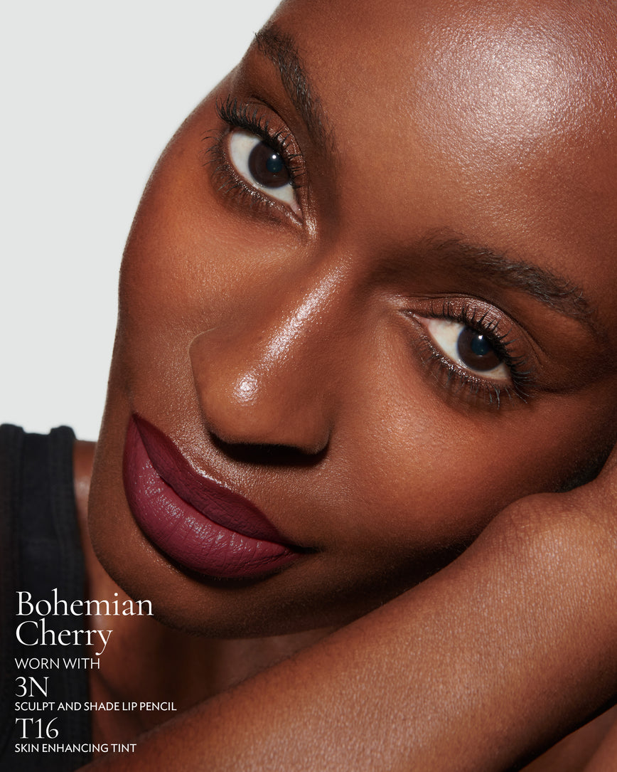 Close-up of a woman with a grey background, focusing on the lip colour - deep claret Bohemian Cherry, with notes on the 3N Sculpt and Shade Pencil and T16 Skin Enhancing Tint