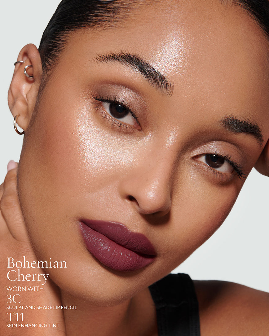 Close-up of a woman with a grey background, focusing on the lip colour - deep claret Bohemian Cherry, with notes on the 3C Sculpt and Shade Pencil and T11 Skin Enhancing Tint