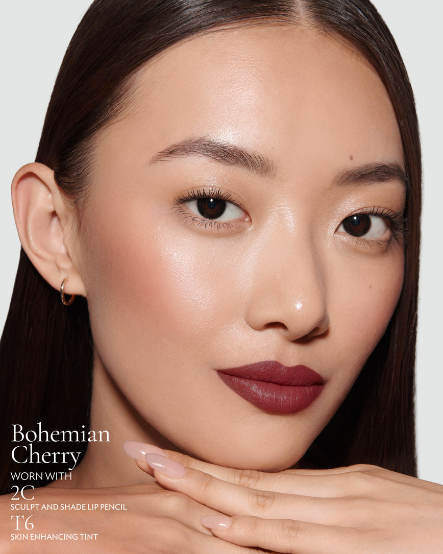 Close-up of a woman with a grey background, focusing on the lip colour - deep claret Bohemian Cherry, with notes on the 2C Sculpt and Shade Pencil and T6 Skin Enhancing Tint