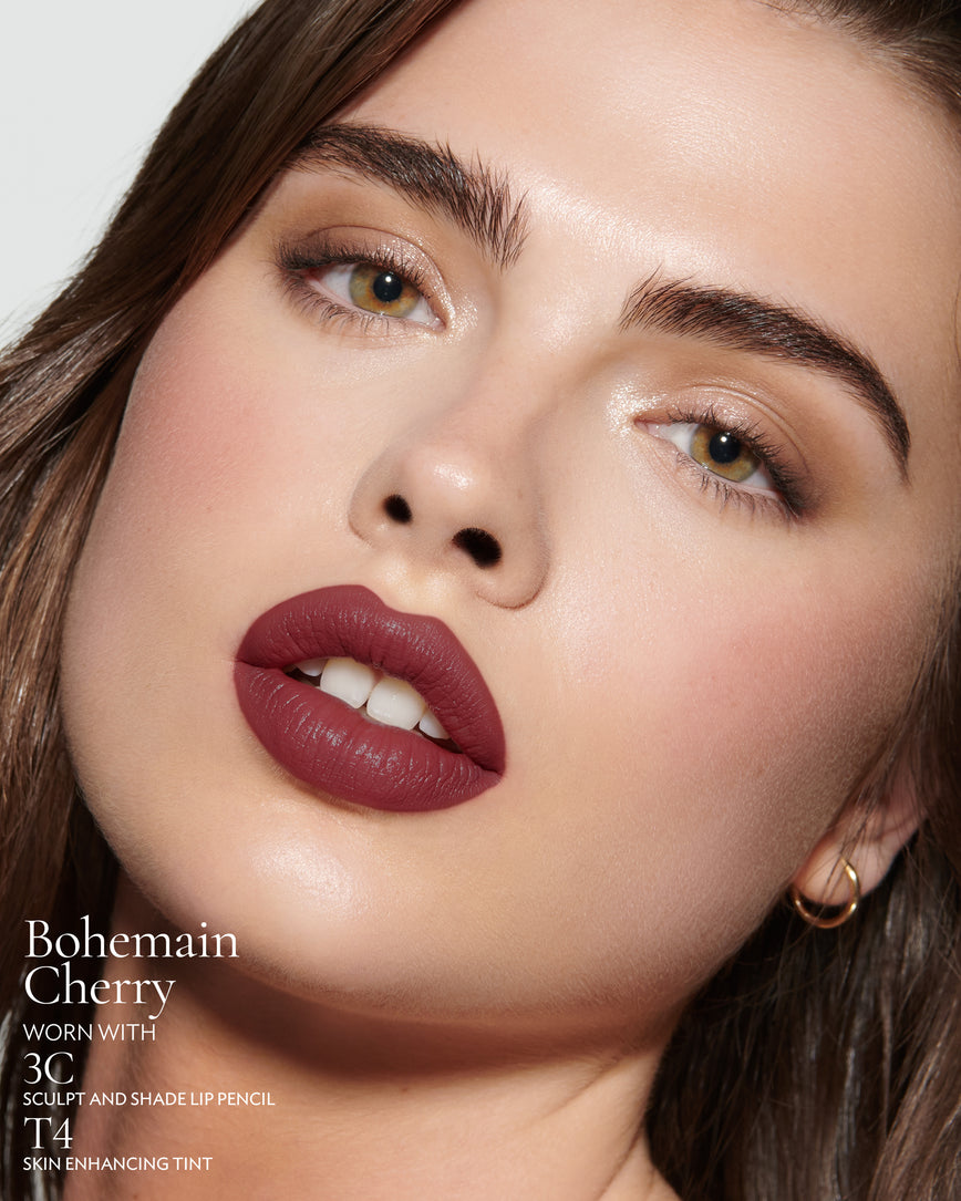 Close-up of a woman with a grey background, focusing on the lip colour - deep claret Bohemian Cherry, with notes on the 3C Sculpt and Shade Pencil and T4 Skin Enhancing Tint