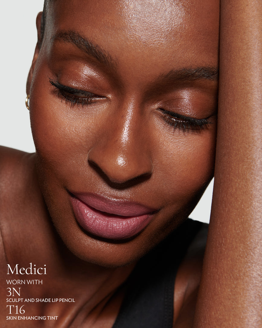 Close-up of a woman with a grey background, focusing on the lip colour - mauve berry Medici, with notes on the 3N Sculpt and Shade Pencil and T16 Skin Enhancing Tint
