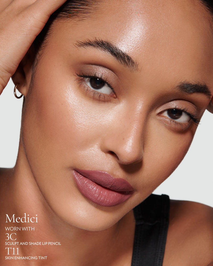 Close-up of a woman with a grey background, focusing on the lip colour - mauve berry Medici, with notes on the 3C Sculpt and Shade Pencil and T11 Skin Enhancing Tint