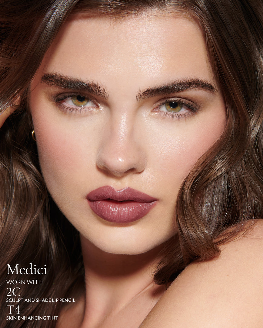Close-up of a woman with a grey background, focusing on the lip colour - mauve berry Medici, with notes on the 2C Sculpt and Shade Pencil and T4 Skin Enhancing Tint