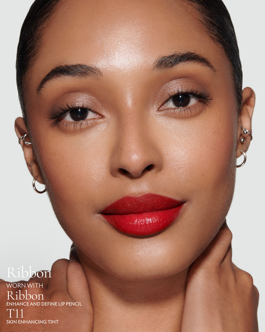 Close-up of a woman with a grey background, focusing on the lip colour - Pillar-box red Ribbon, with notes on the Ribbon Enhance and Define Pencil and T11 Skin Enhancing Tint
