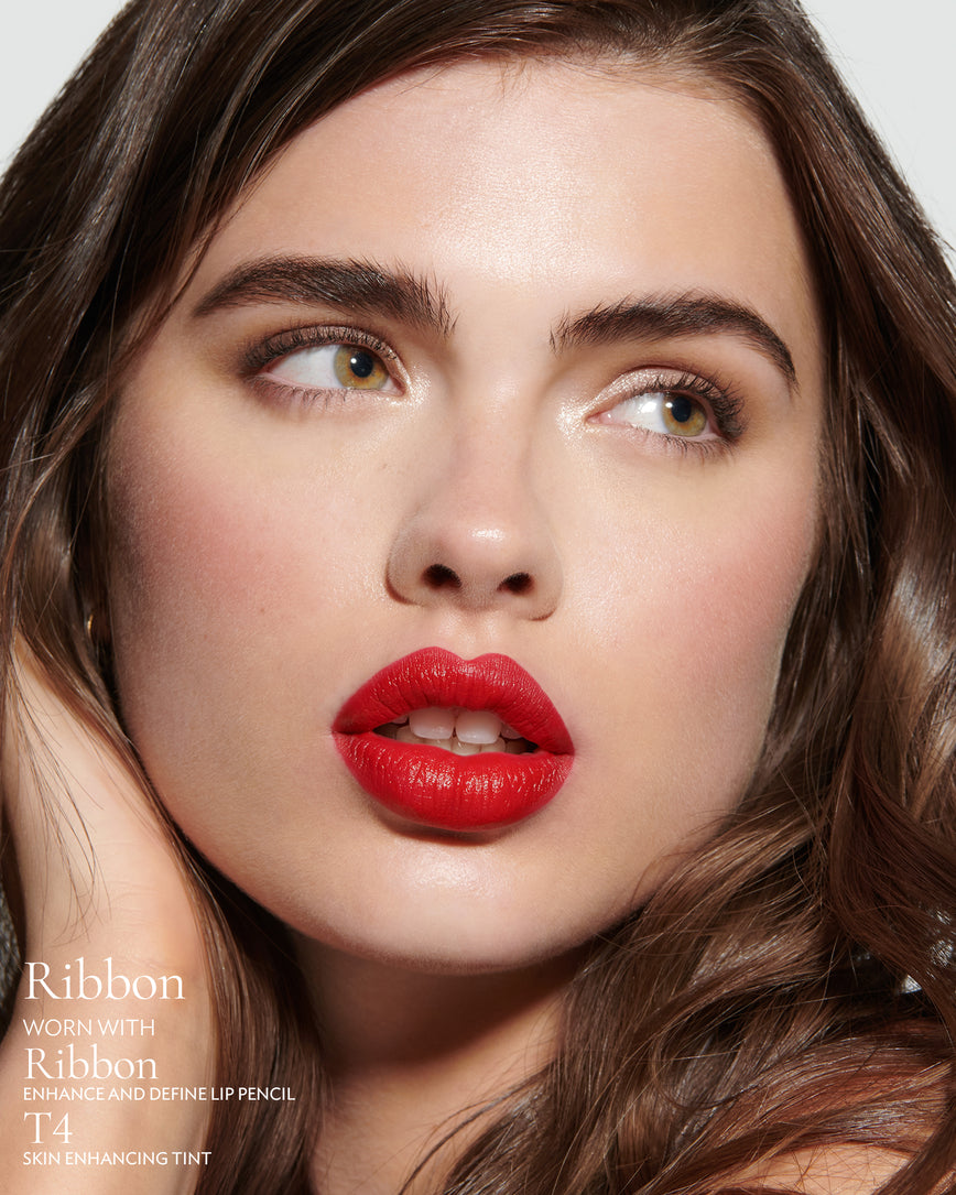 Close-up of a woman with a grey background, focusing on the lip colour - Pillar-box red Ribbon, with notes on the Ribbon Enhance and Define Pencil and T4 Skin Enhancing Tint