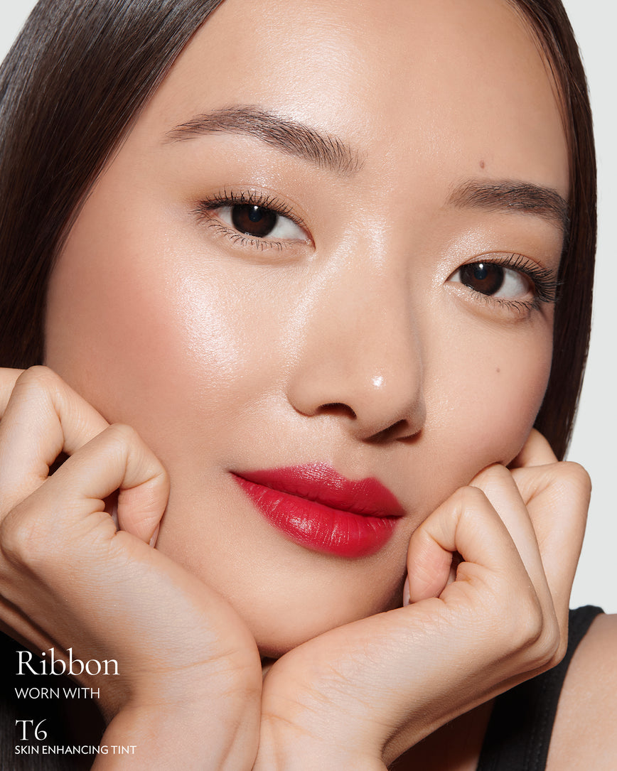 Close-up of a woman with a grey background, focusing on the lip colour - Pillar-box red Ribbon, with notes on T11 Skin Enhancing Tint