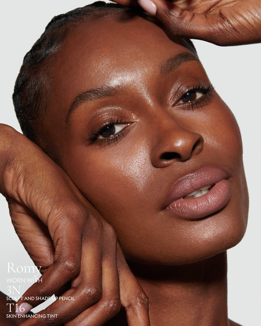 Close-up of a woman with a grey background, focusing on the lip colour - muted heather Romy, with notes on the 3N Sculpt and Shade Pencil and T16 Skin Enhancing Tint