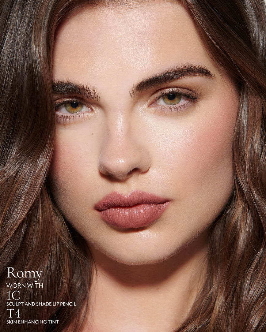 Close-up of a woman with a grey background, focusing on the lip colour - muted heather Romy, with notes on the 1C Sculpt and Shade Pencil and T4 Skin Enhancing Tint