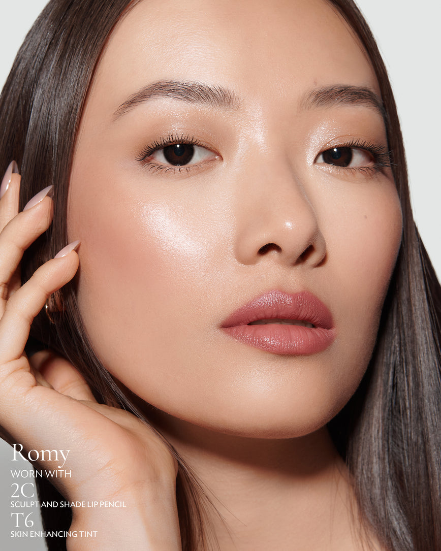 Close-up of a woman with a grey background, focusing on the lip colour - muted heather Romy, with notes on the 2C Sculpt and Shade Pencil and T6 Skin Enhancing Tint