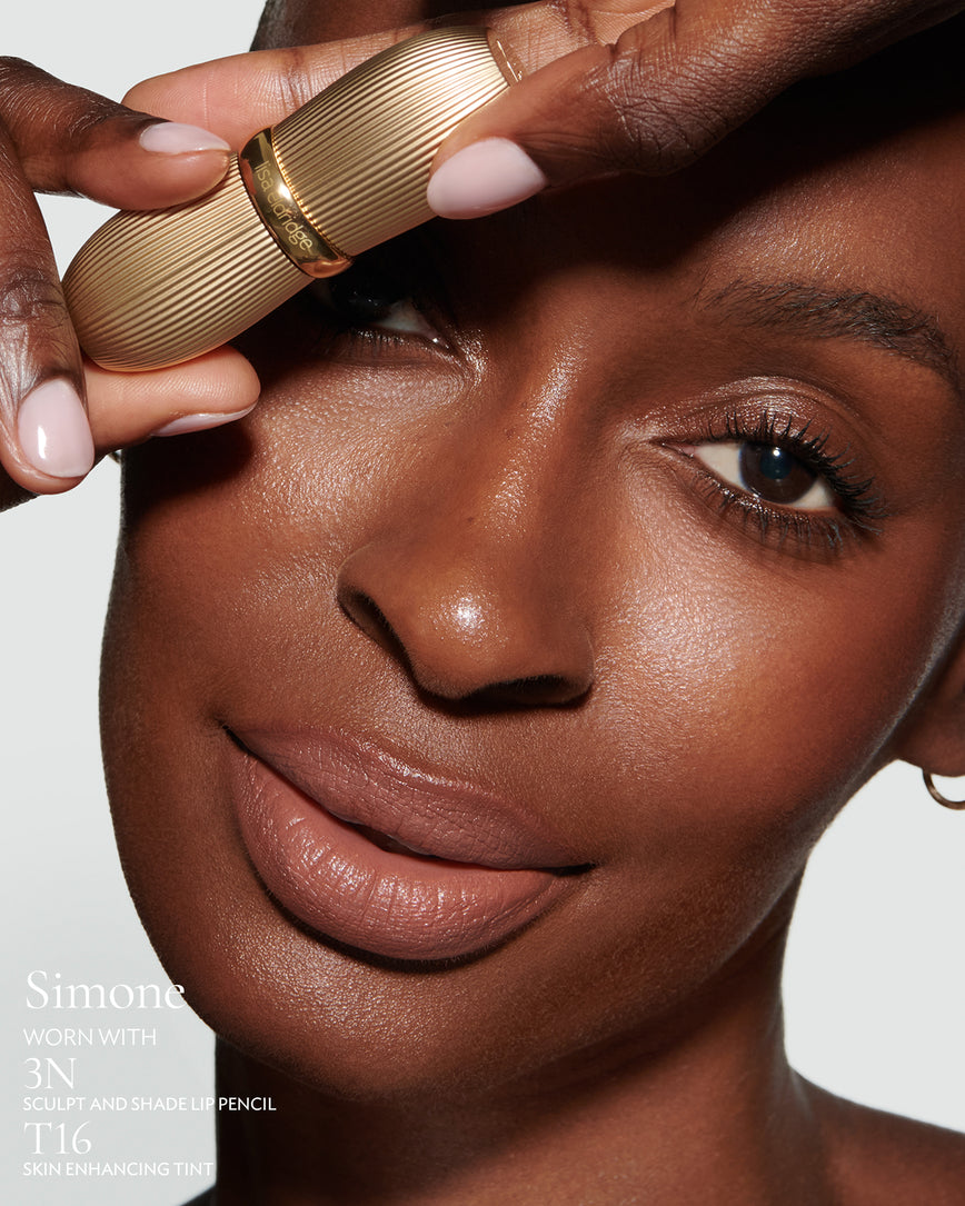Close-up of a woman with a grey background, focusing on the lip colour - tawny caramel Simone, with notes on the 3N Sculpt and Shade Pencil and T16 Skin Enhancing Tint