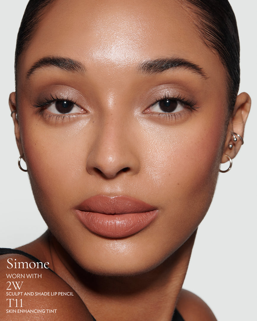 Close-up of a woman with a grey background, focusing on the lip colour - tawny caramel Simone, with notes on the 2W Sculpt and Shade Pencil and T11 Skin Enhancing Tint