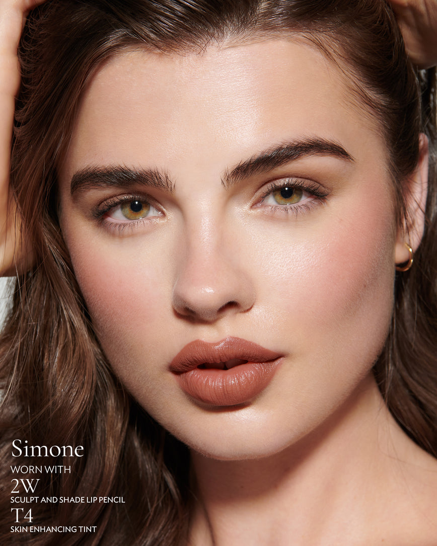 Close-up of a woman with a grey background, focusing on the lip colour - tawny caramel Simone, with notes on the 2W Sculpt and Shade Pencil and T4 Skin Enhancing Tint
