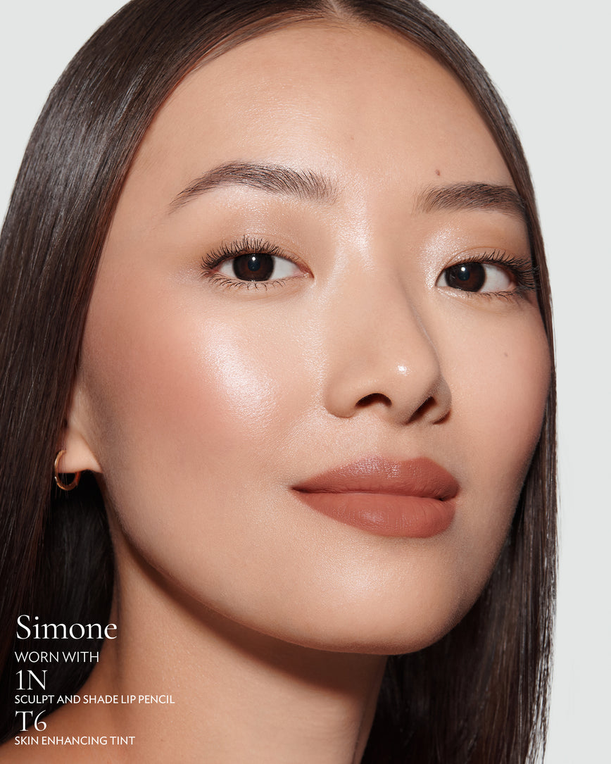 Close-up of a woman with a grey background, focusing on the lip colour - tawny caramel Simone, with notes on the 1N Sculpt and Shade Pencil and T6 Skin Enhancing Tint