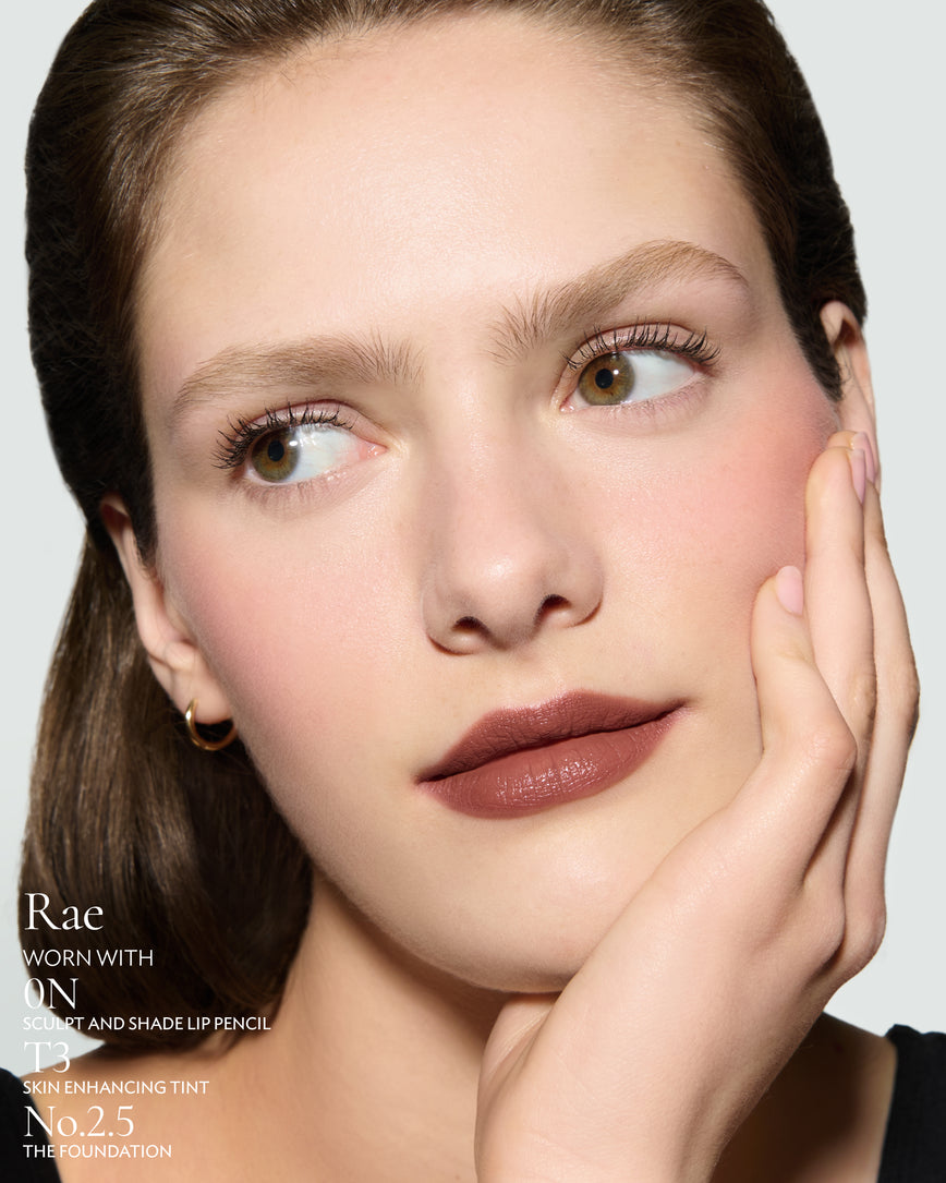 Close-up of a woman's face on a plain background. Woman is wearing Rae Rouge Experience, 0N Sculpt Pencil, T3 Skin Tint and 2.5 Foundation