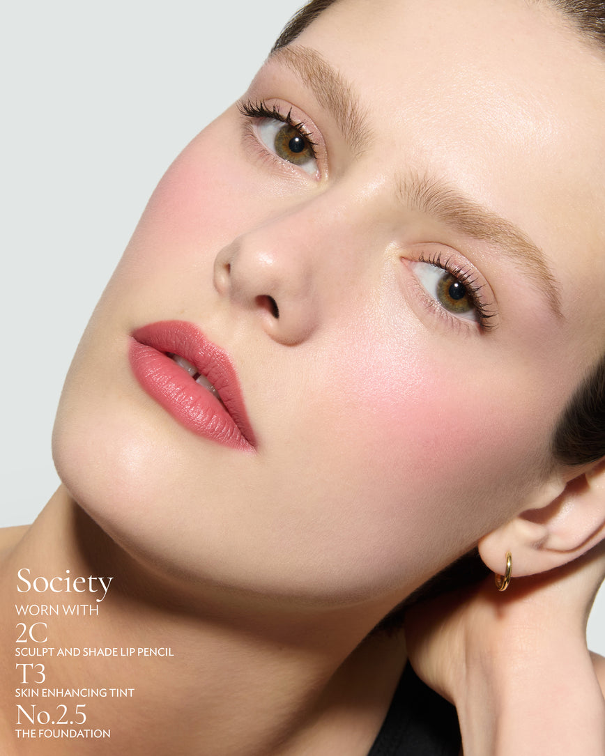 Close-up of a woman with a grey background, focusing on the lip colour - warm pink Society, with notes on the 2C Sculpt and Shade Pencil and T3 Skin Enhancing Tint and 2.5 Foundation