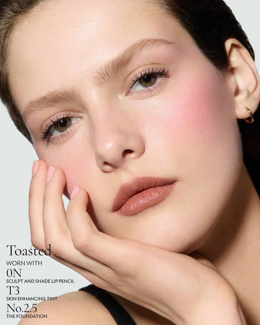 Close-up of a woman with a grey background, focusing on the lip colour - neutral-beige Toasted, with notes on the 0N Sculpt and Shade Pencil and T3 Skin Enhancing Tint and 2.5 Foundation