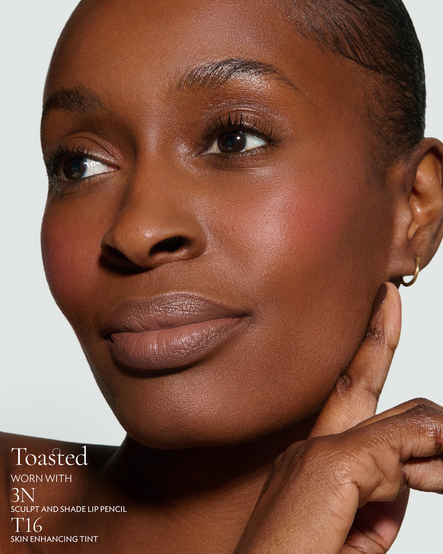Close-up of a woman with a grey background, focusing on the lip colour - neutral-beige Toasted, with notes on the 3N Sculpt and Shade Pencil and T16 Skin Enhancing Tint 