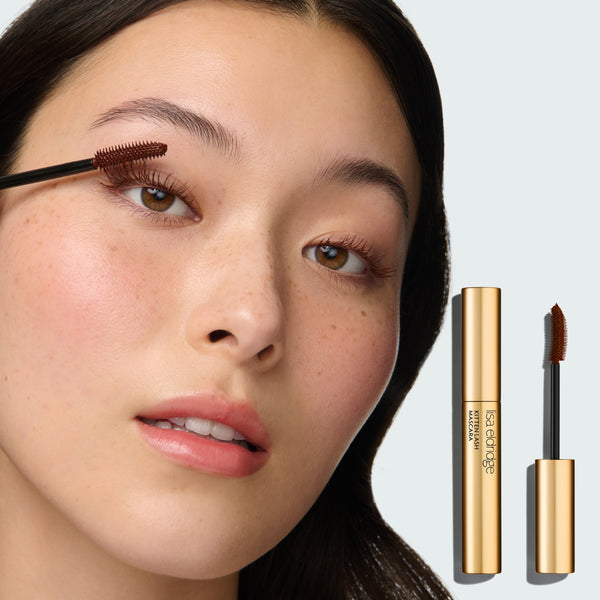 Close-up of a model's face, applying Kitten Lash Mascara, with the product pack in the foreground on a neutral background