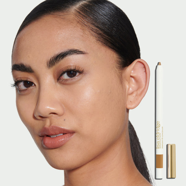 Close-up of a model's face wearing Pinpoint Concealer with the product pack in the foreground on a neutral background