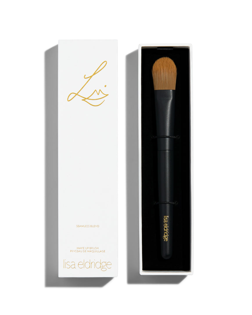 handle and a flat rounded brush. The lid of the box sits next to the bottom and has the Lisa Eldridge logo in gold as well as the text, ‘SEAMLESS BLEND MAKE UP BRUSH PINCEAU DE MAQUILLAGE lisa eldridge’ 