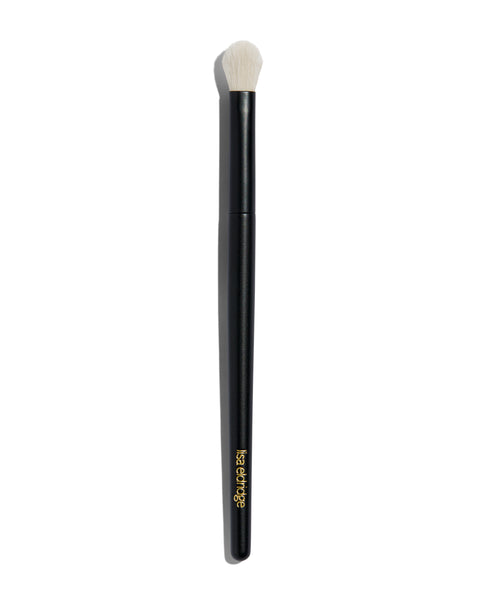 Foundation brush with a long black handle and a short rounded tip with white bristles. The handle says ‘lisa eldridge’ in gold at the bottom