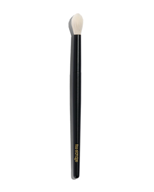 Foundation brush with a long black handle and a rounded tip with long, tapered white bristles. The handle says ‘lisa eldridge’ in gold at the bottom