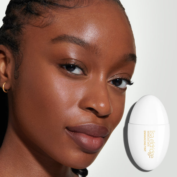 Close-up of a model's face, wearing Seamless Skin Enhancing Tint, with the product pack in the foreground on a neutral background