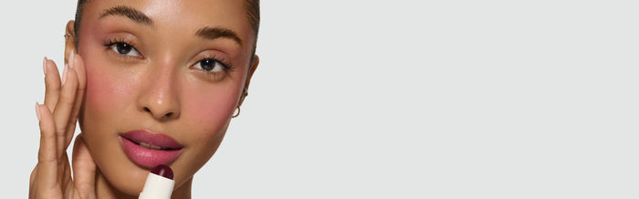 Model applying Hellebore Heaven Velatura Lip and Cheek Stick to cheek,  with a neutral background