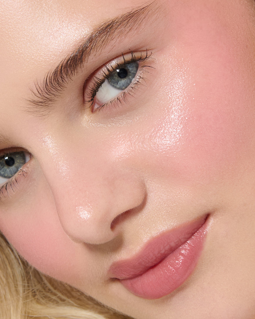 Close-up of a model's face with a neutral background, wearing Rose Madder Velatura Balm on lip and cheeks 