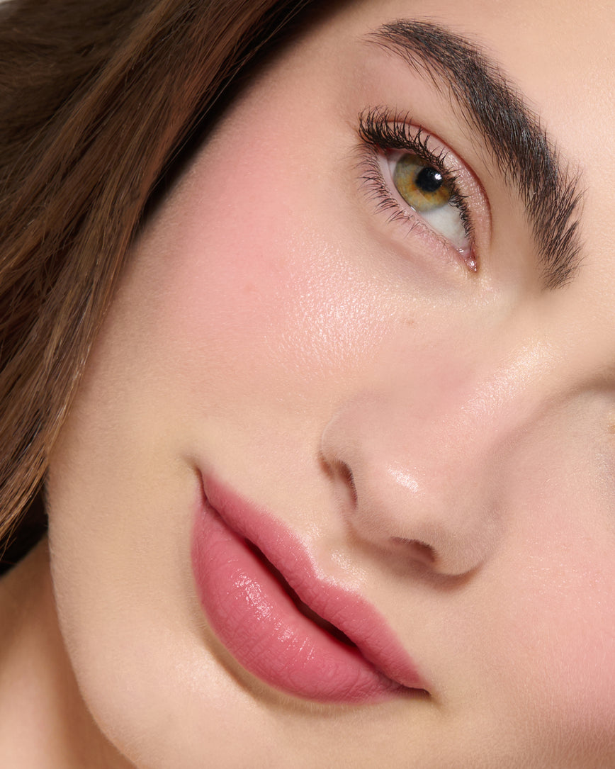 Close-up of a model's face with a neutral background, wearing Rose Madder Velatura Balm on lip and cheeks 