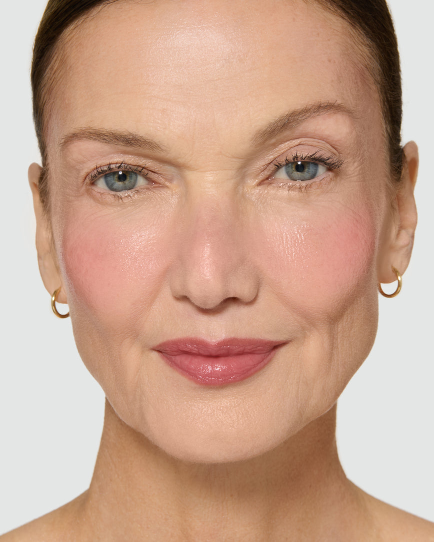 Close-up of a model's face with a neutral background, wearing Velatura Balm in shade Rose Madder