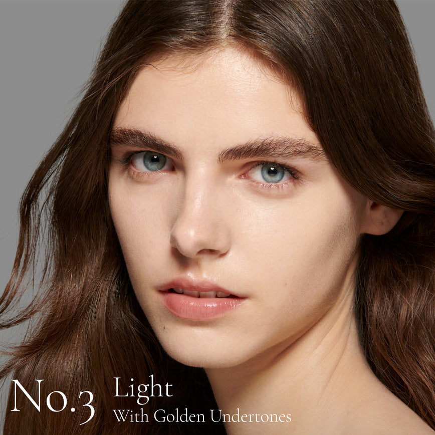 Lisa Eldridge Seamless Skin Foundation Pictured on Model. The model has light skin, blue eyes and dark chestnut hair and eyebrows. The Text says ' No. 3 Light With Golden Undertones'