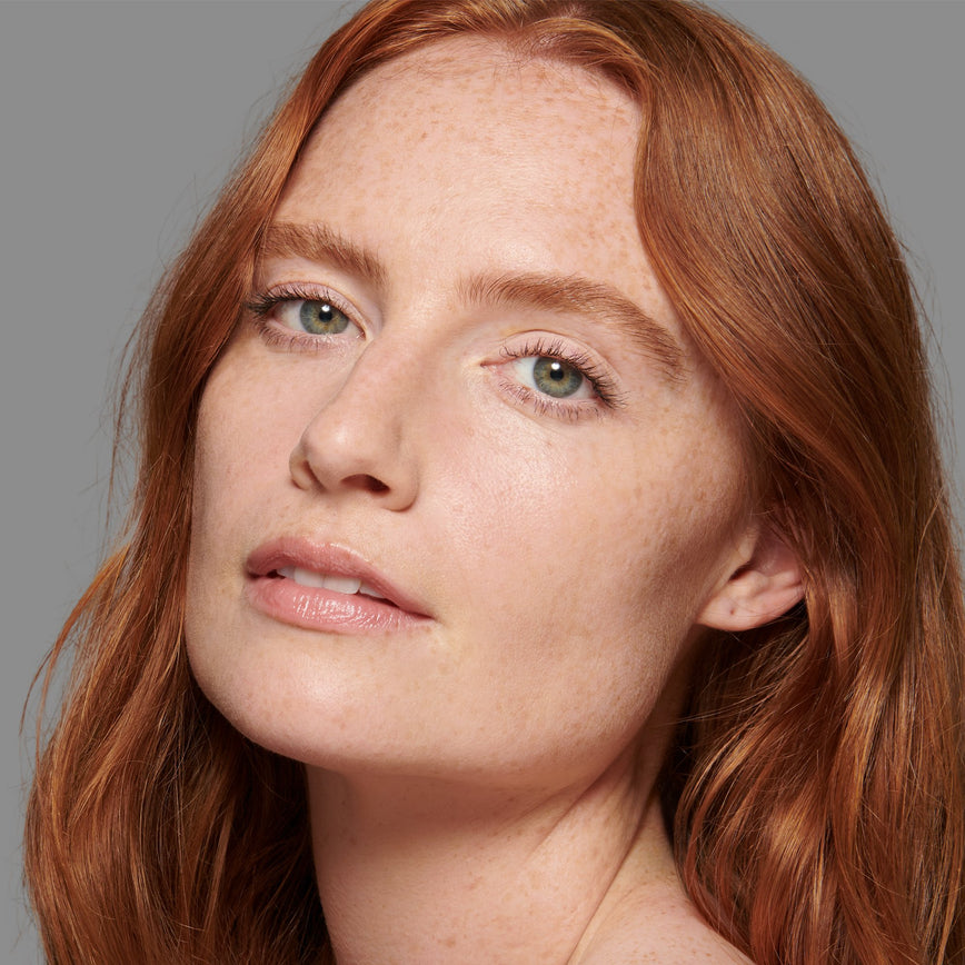 Lisa Eldridge Seamless Skin Foundation Pictured on Model. A young model with light skin and neutral undertones, green eyes and red, slightly wavy, hair.