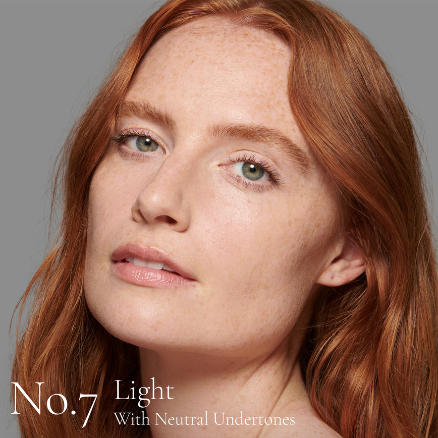 Lisa Eldridge Seamless Skin Foundation Pictured on Model. A young model with light skin and neutral undertones, green eyes and red, slightly wavy, hair. The text says ‘No.7 Light With Neutral Undertones'